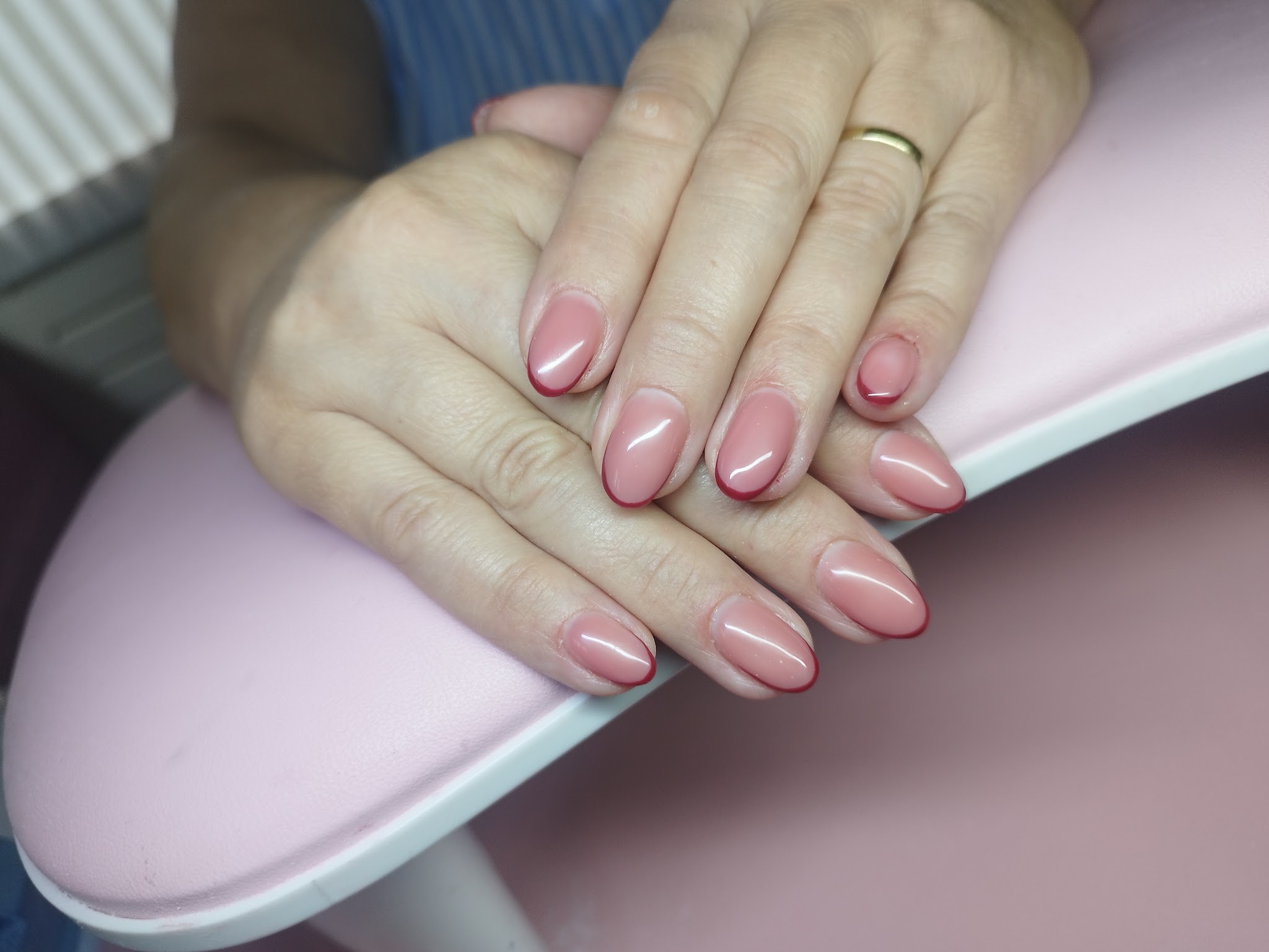 Amandelvormige roze gelnagels met een fijn rood lijntje langs de rand, op een roze handsteun