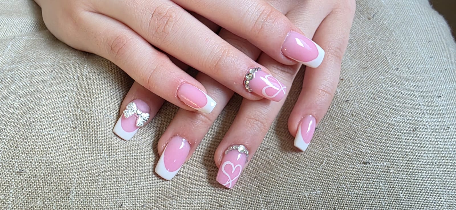 Roze French nagels met witte strikjes op linnen