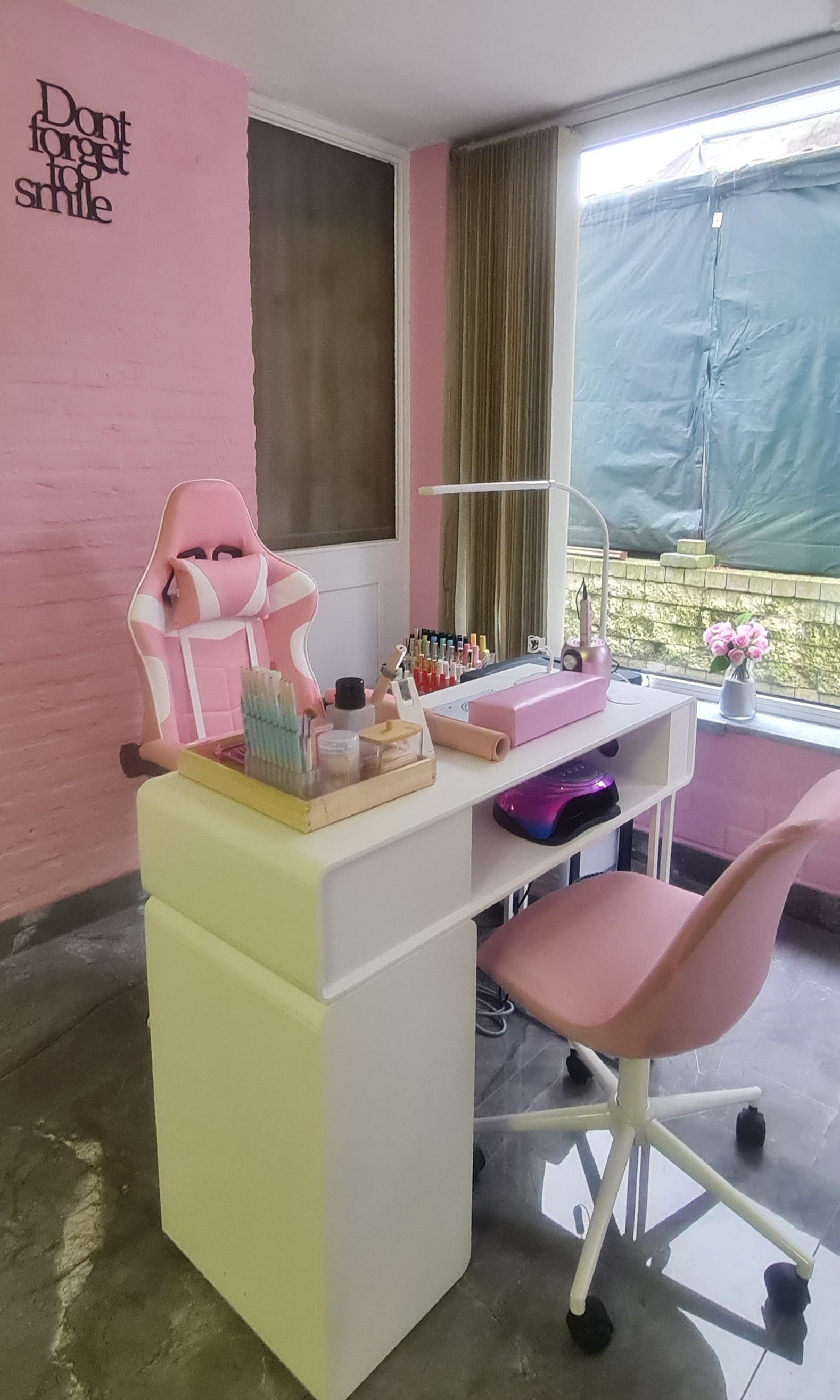 De roze nagelstudio: witte manicuretafel, roze stoelen en de tekst Dont forget to smile op de muur